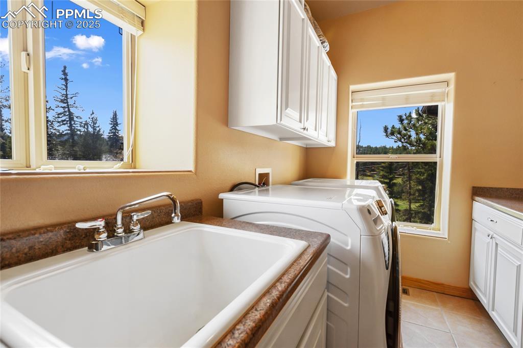The laundry area features a washing machine and dryer, light tiled flooring, cabinetry, and a sink. 