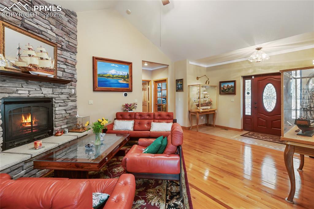 Living room with high vaulted ceiling, wood finished floors, a fireplace, overlooking the entryway, and crown molding.
