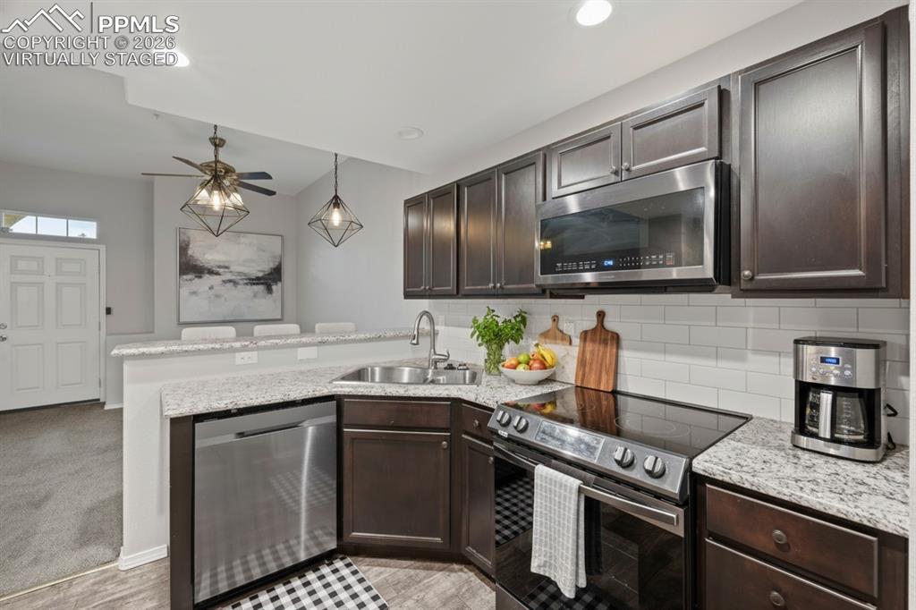 Kitchen featuring stainless steel appliances, dark brown cabinetry, recessed lighting, granite countertops, and baseboards. This photo is virtually staged.