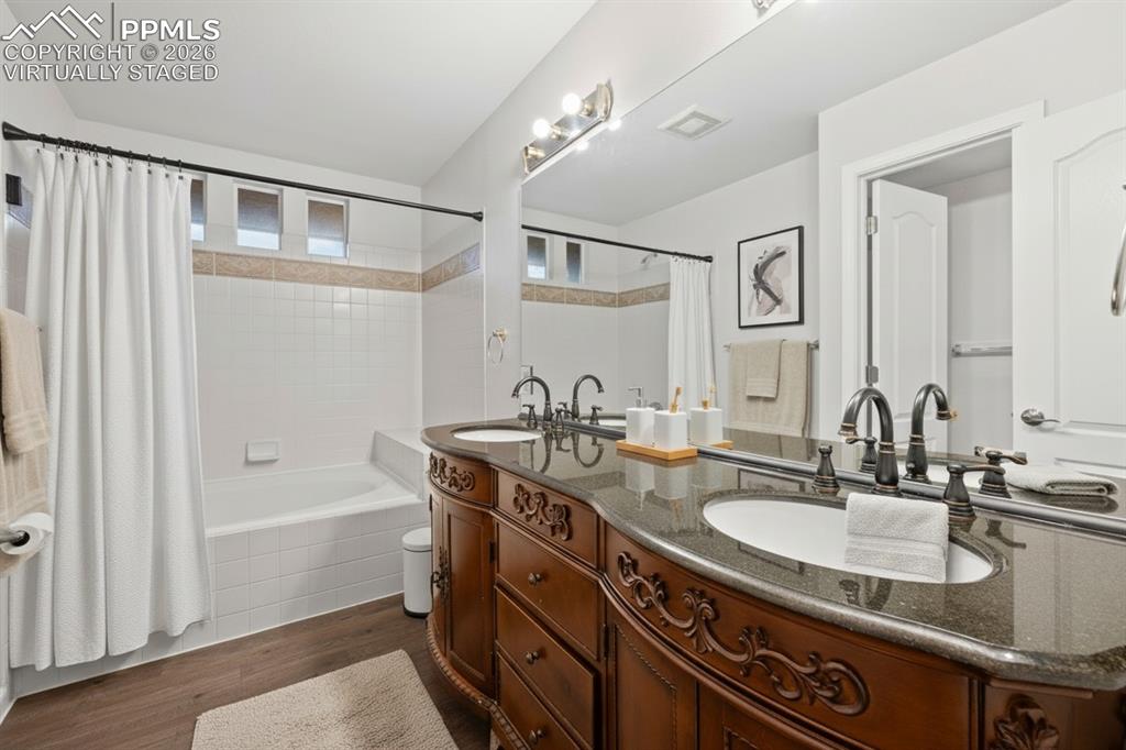 Full bath with double vanity, shower / bathtub combination with curtain, and wood finished floors. This photo is virtually staged.