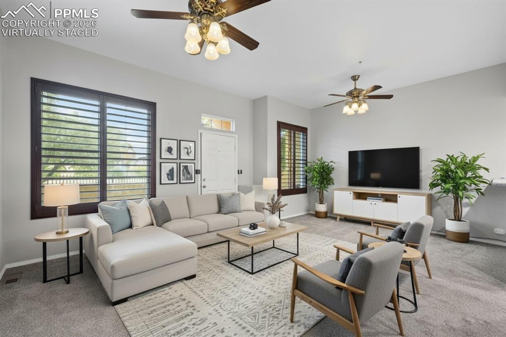 Living room featuring custom window shutters, a ceiling fan, carpet flooring, stairway, and a glass covered fireplace. This photo is virtually staged
.