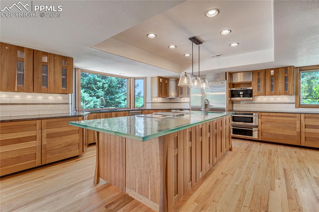 Kitchen featuring glass insert cabinets, decorative backsplash, a tray ceiling, a spacious island, and recessed lighting
