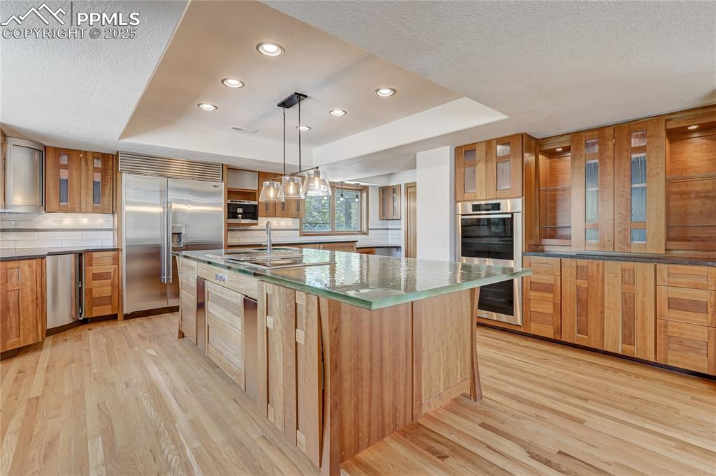 Kitchen featuring a raised ceiling, glass insert cabinets, decorative light fixtures, recessed lighting, and light wood finished floors