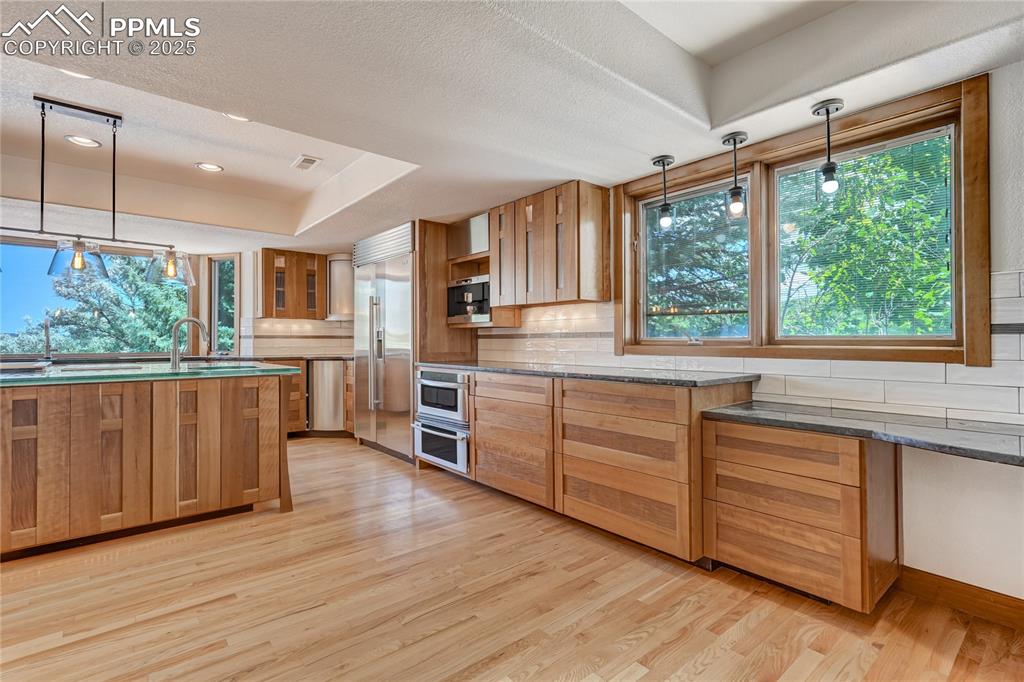 Kitchen with decorative light fixtures, tasteful backsplash, light wood finished floors, stainless steel appliances, and brown cabinetry