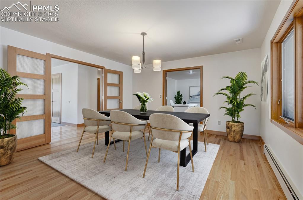 Dining space with baseboard heating, light wood-style flooring, and a chandelier, virtually staged