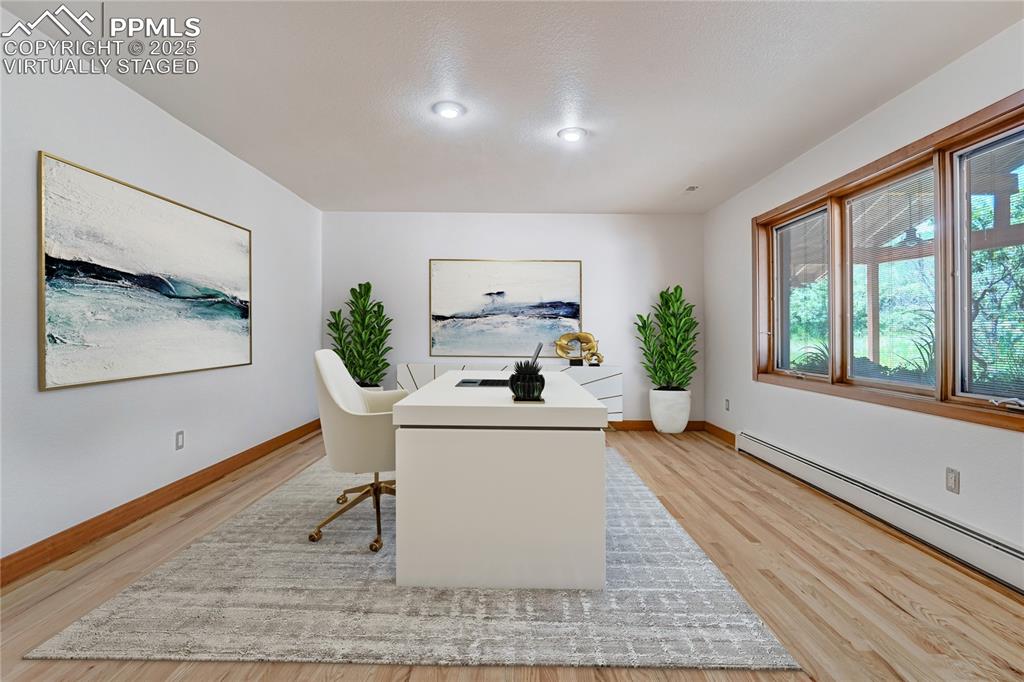 Office area with light wood-type flooring and baseboard heating, virtually staged