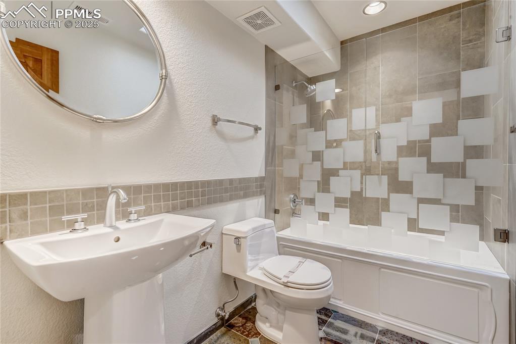 Full bathroom with a textured wall, shower / washtub combination, tile walls, and recessed lighting