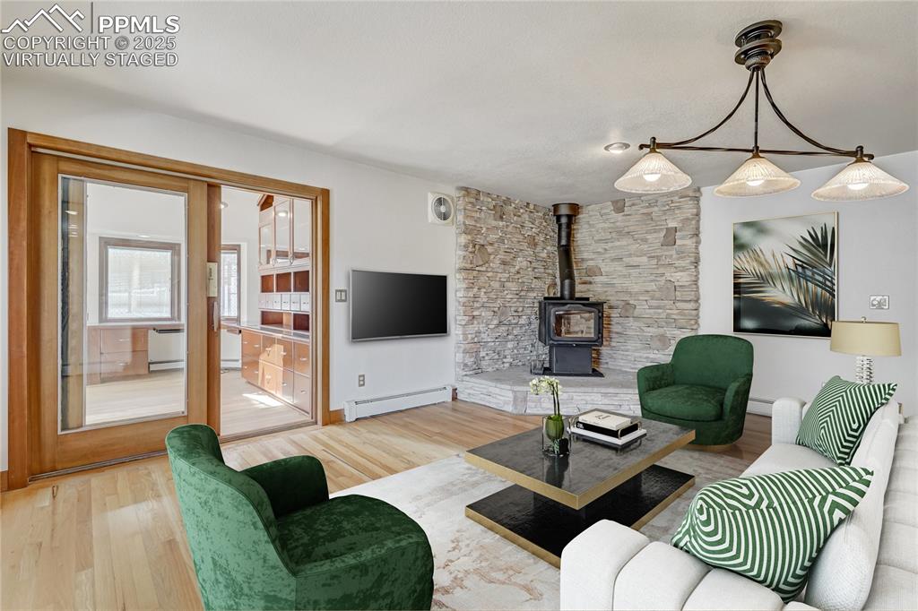 Living area featuring a wood stove, wood finished floors, and a baseboard heating unit, virtually staged