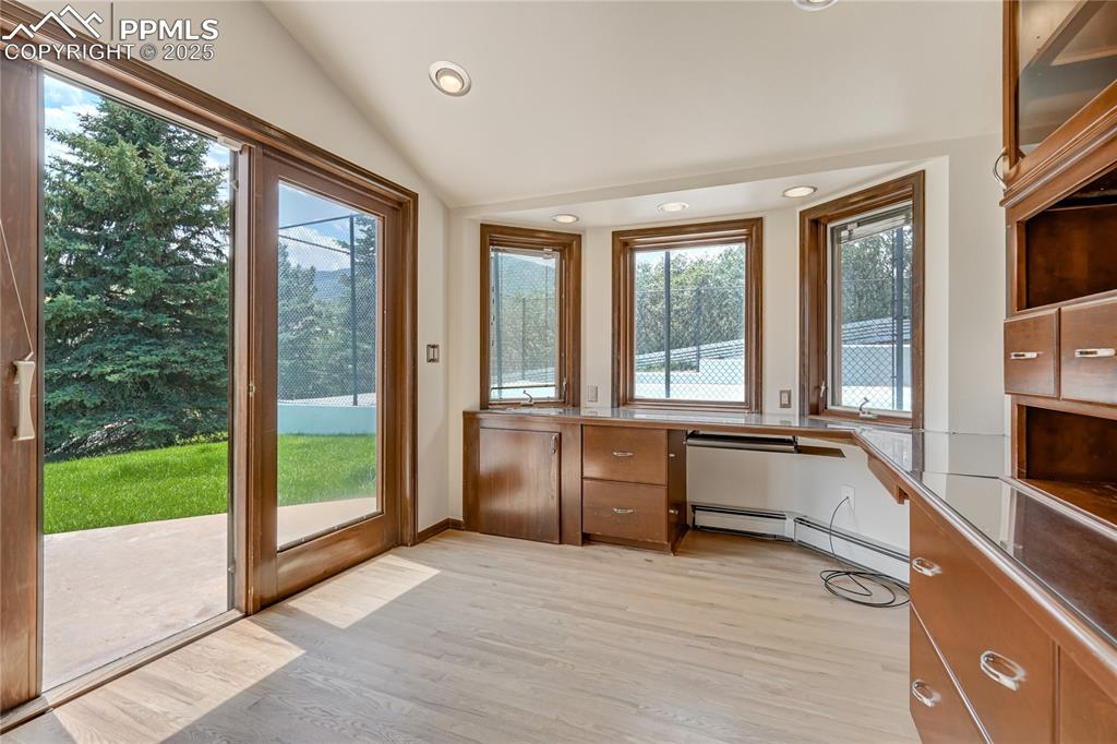 Doorway with built in desk, recessed lighting, lofted ceiling, wood finished floors, and a baseboard heating unit