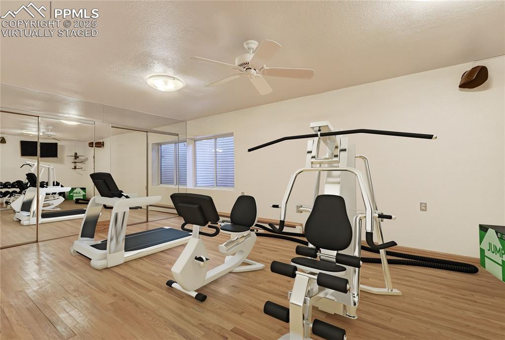 Workout area featuring a textured ceiling, light wood-type flooring, and ceiling fan, virtually staged
