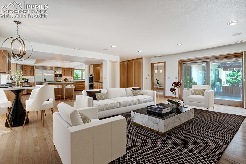 Living area featuring light wood-style floors, recessed lighting, and a chandelier, virtually staged