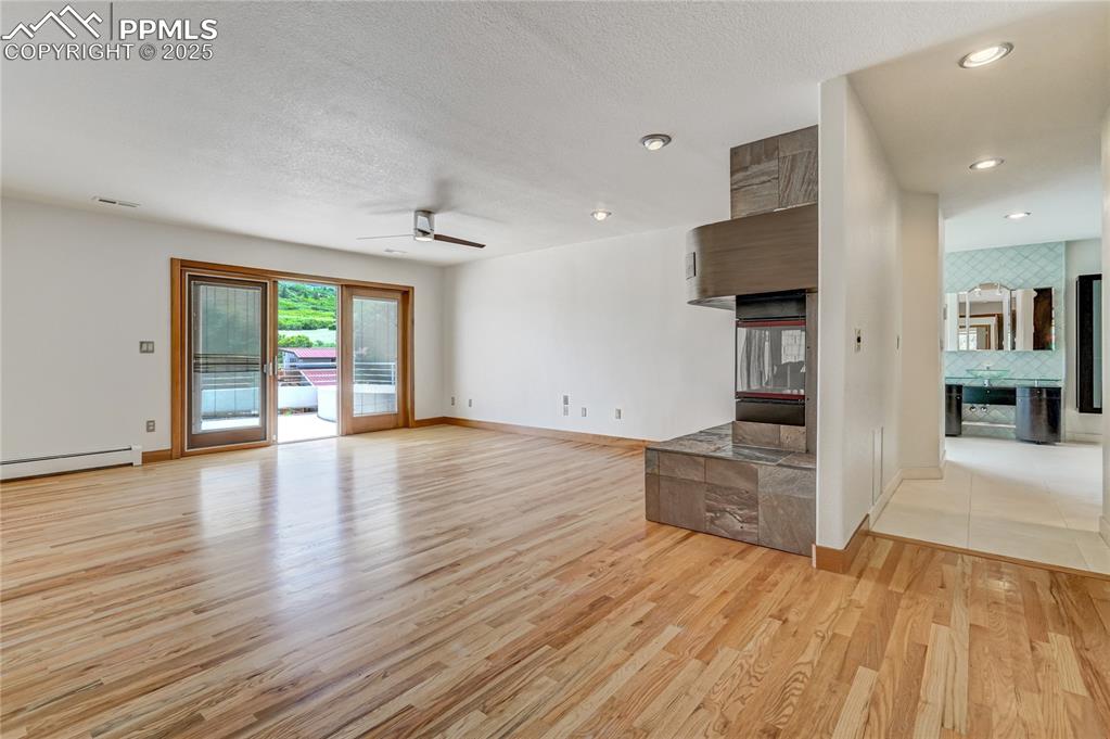 Unfurnished living room with light wood finished floors, ceiling fan, a textured ceiling, a baseboard heating unit, and recessed lighting