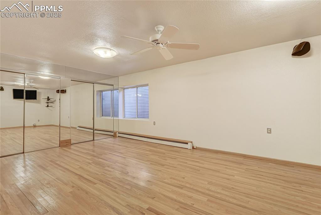 Unfurnished bedroom featuring wood-type flooring, a textured ceiling, a closet, a ceiling fan, and a baseboard heating unit
