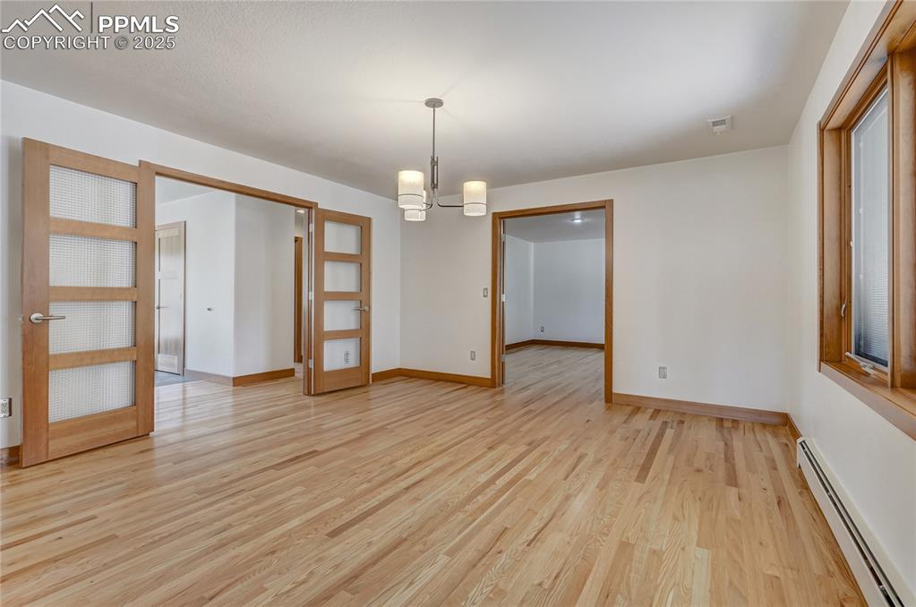 Unfurnished room with baseboard heating, a chandelier, and light wood finished floors