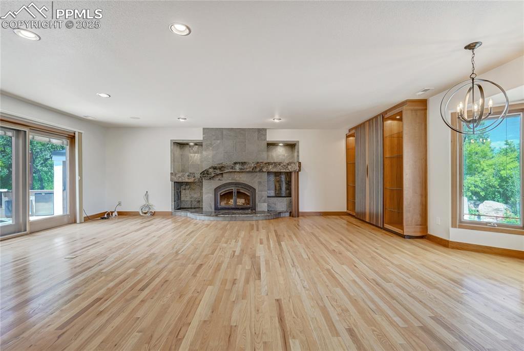 Unfurnished living room with a tiled fireplace, light wood-style flooring, recessed lighting, and a chandelier