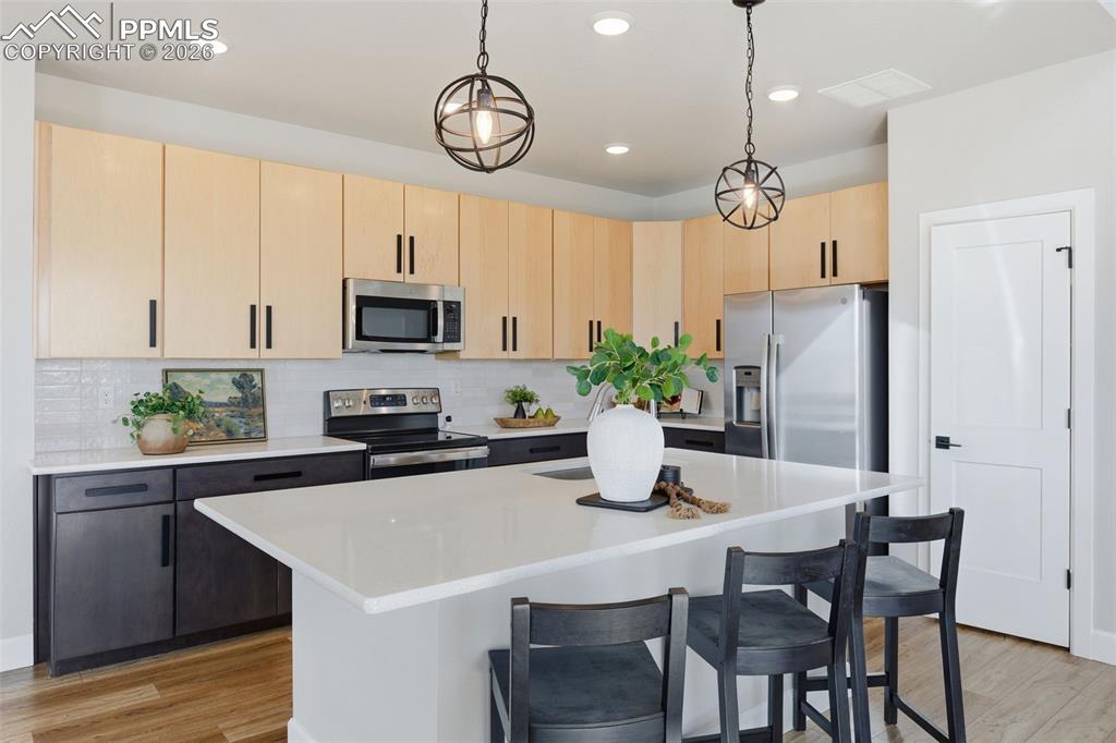 Kitchen with light wood finish cabinetry, stainless steel appliances, decorative light fixtures, and decorative backsplash