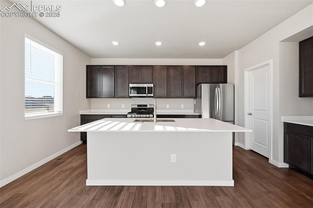 Kitchen with dark wood finish cabinets, stainless steel appliances, a center island with sink, dark wood finished floors, and recessed lighting