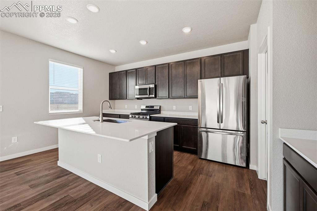 Kitchen featuring stainless steel appliances, dark wood finish cabinets, a kitchen island with sink, dark wood-style floors, and recessed lighting