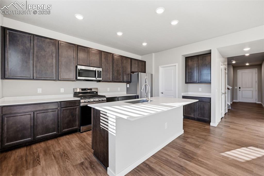 Kitchen with stainless steel appliances, recessed lighting, a kitchen island with sink, dark wood finished floors, and dark wood finish cabinets