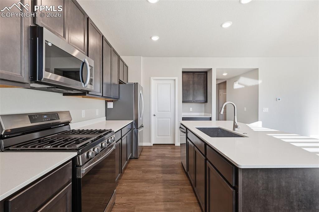 Kitchen featuring stainless steel appliances, dark wood finish cabinetry, a center island with sink, dark wood-style flooring, and recessed lighting