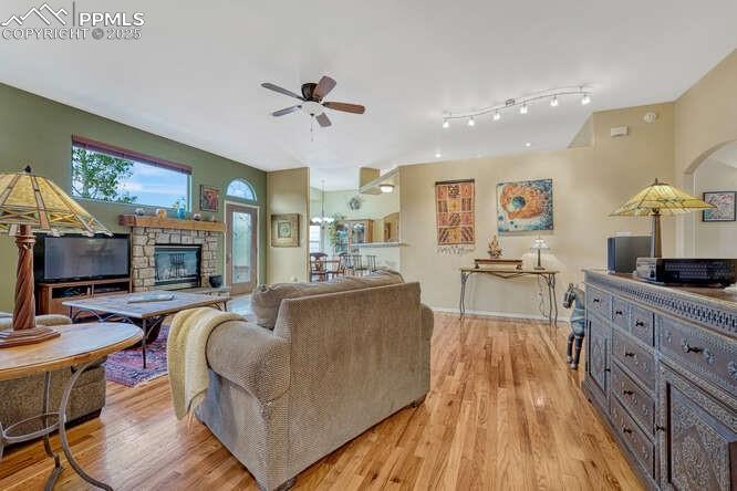 Living area featuring light wood-style flooring, a ceiling fan, a stone fireplace, and rail lighting