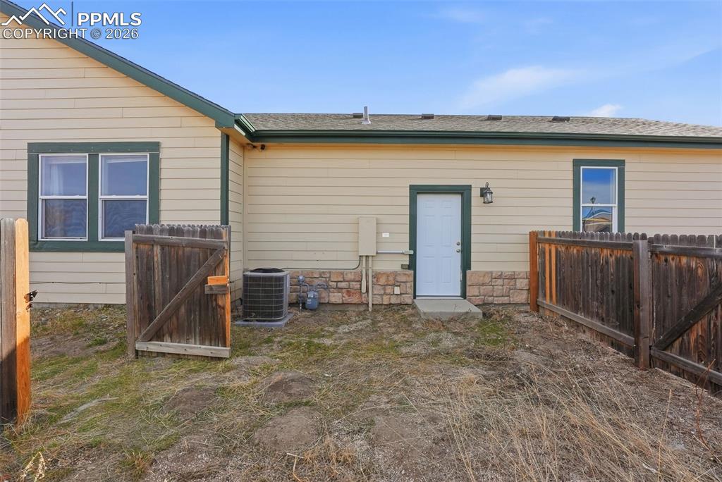 Back of property with a gate, stone siding, and a shingled roof
