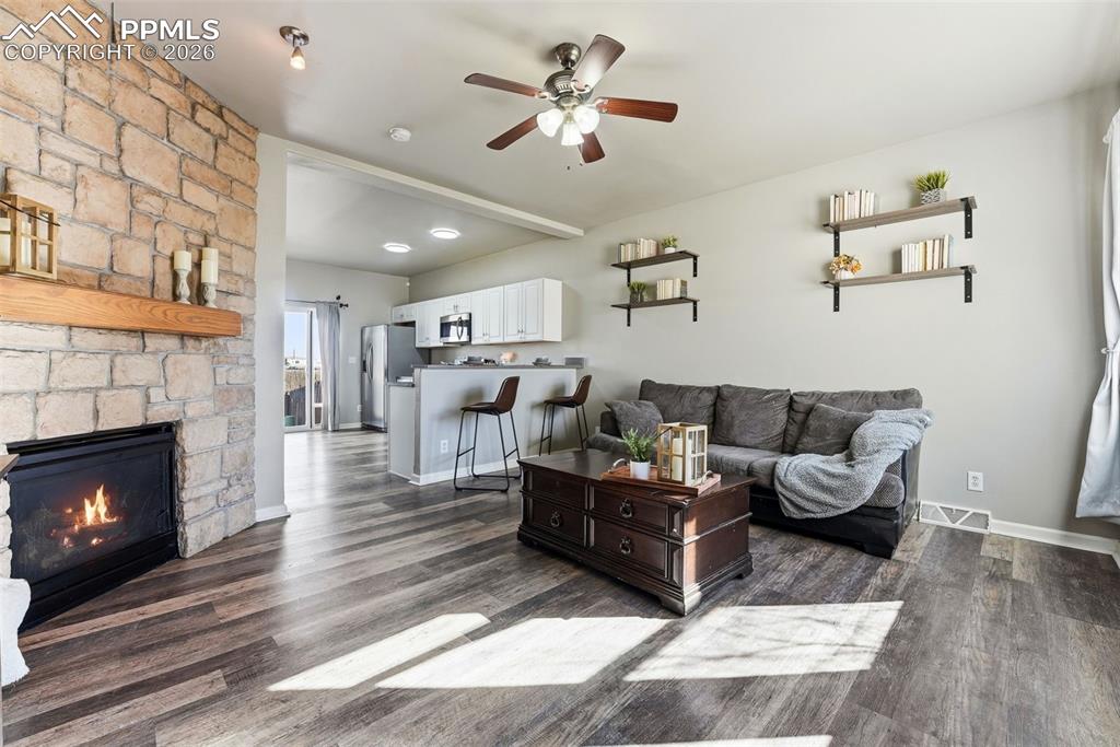 Living area with a ceiling fan, dark wood-type flooring, and a stone fireplace