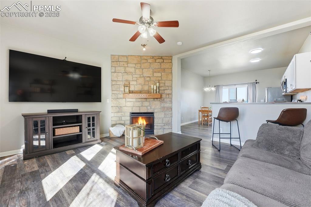 Living room with ceiling fan, a stone fireplace, and dark wood-type flooring