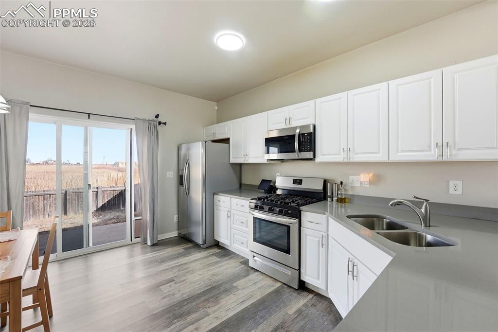 Kitchen featuring stainless steel appliances, white cabinets, light wood-style flooring, and light stone countertops