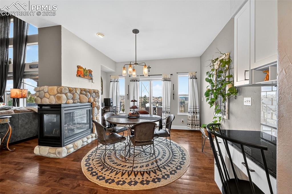Dining space featuring dark wood-style flooring, a stone fireplace, and a chandelier