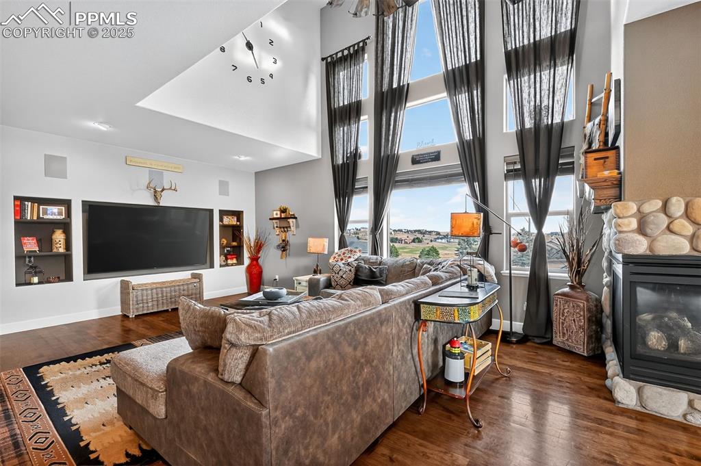 Living room featuring a towering ceiling, wood finished floors, and a stone fireplace