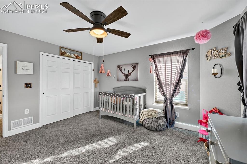 Bedroom featuring a crib, carpet flooring, a closet, and a ceiling fan
