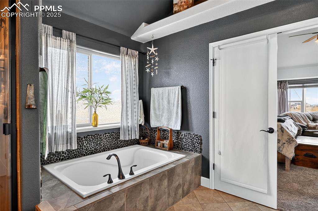 Bathroom featuring a garden tub, light tile patterned flooring, ensuite bathroom, a textured wall, and ceiling fan