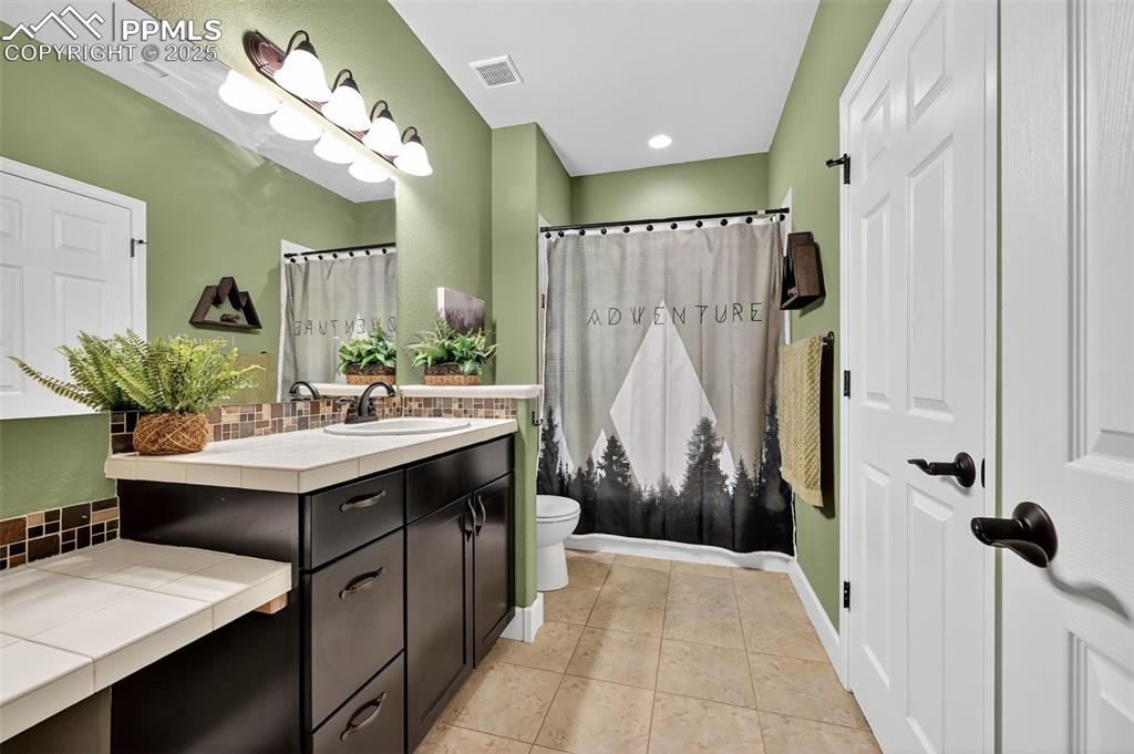 Full bathroom featuring decorative backsplash, vanity, light tile patterned flooring, and shower / tub combo
