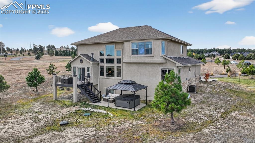 Rear view of house featuring a hot tub, a patio, stucco siding, stairs, and a gazebo