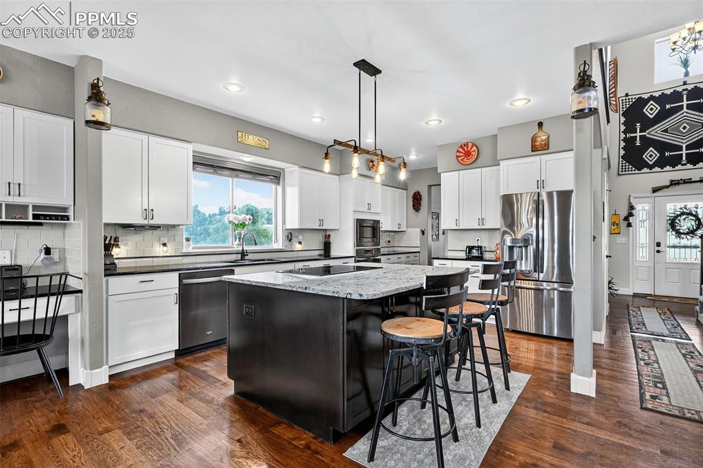 Kitchen featuring tasteful backsplash, appliances with stainless steel finishes, dark wood-style flooring, decorative light fixtures, and a kitchen breakfast bar