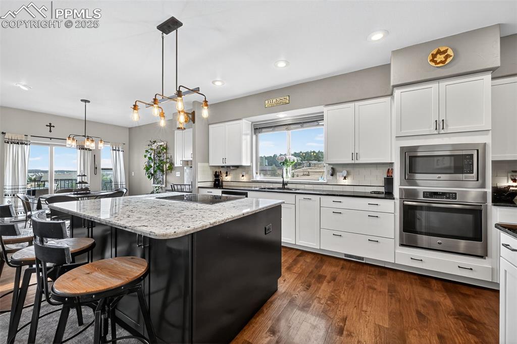Kitchen with a kitchen breakfast bar, stainless steel appliances, dark wood finished floors, decorative backsplash, and recessed lighting