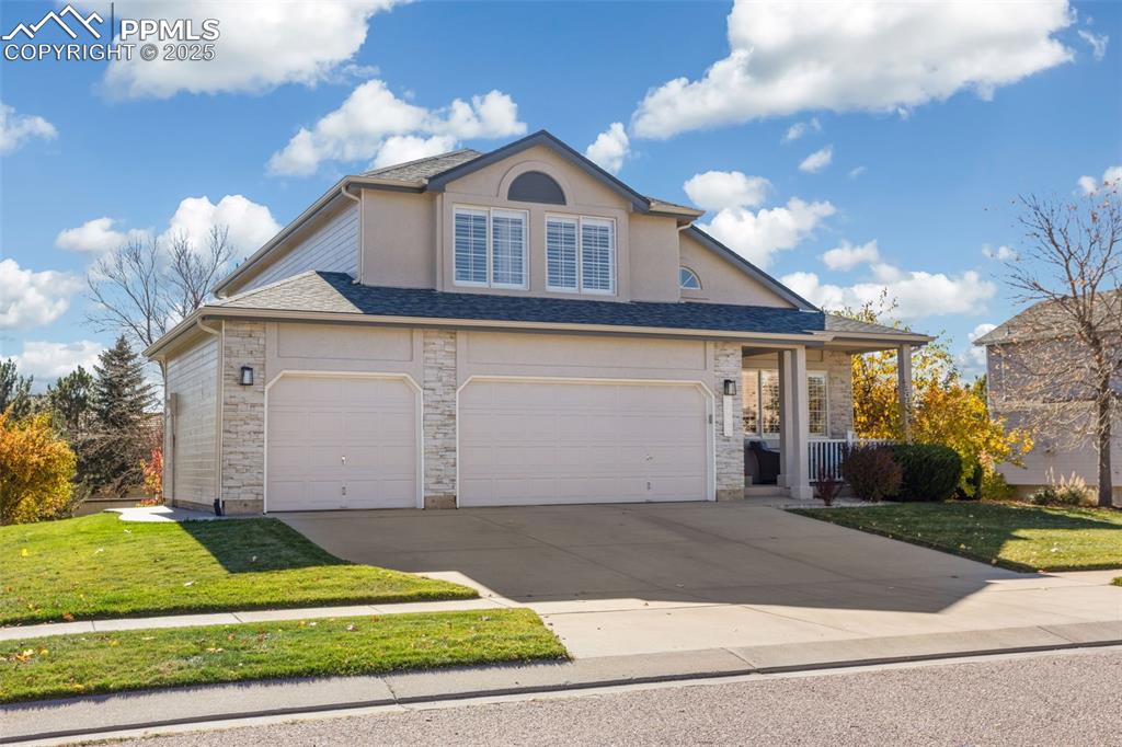 Traditional home with a front yard, concrete driveway, a garage, stone siding, and roof with shingles