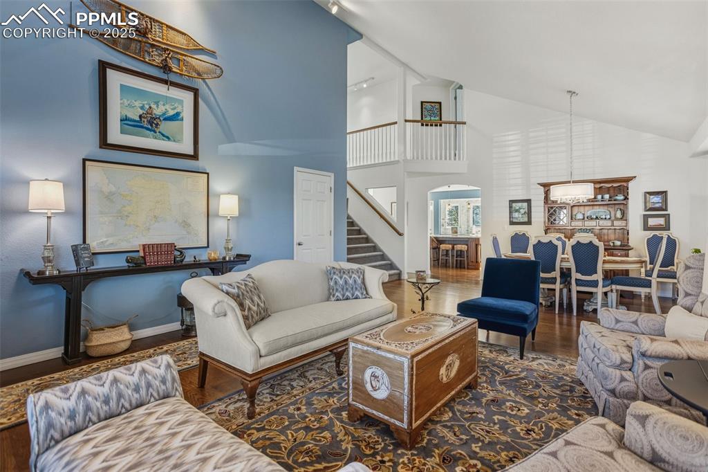 Living room featuring track lighting, dark wood-type flooring, high vaulted ceiling, arched walkways, and stairway
