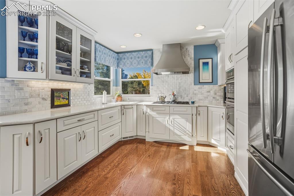 Kitchen with appliances with stainless steel finishes, dark wood finished floors, white cabinets, wall chimney exhaust hood, and recessed lighting