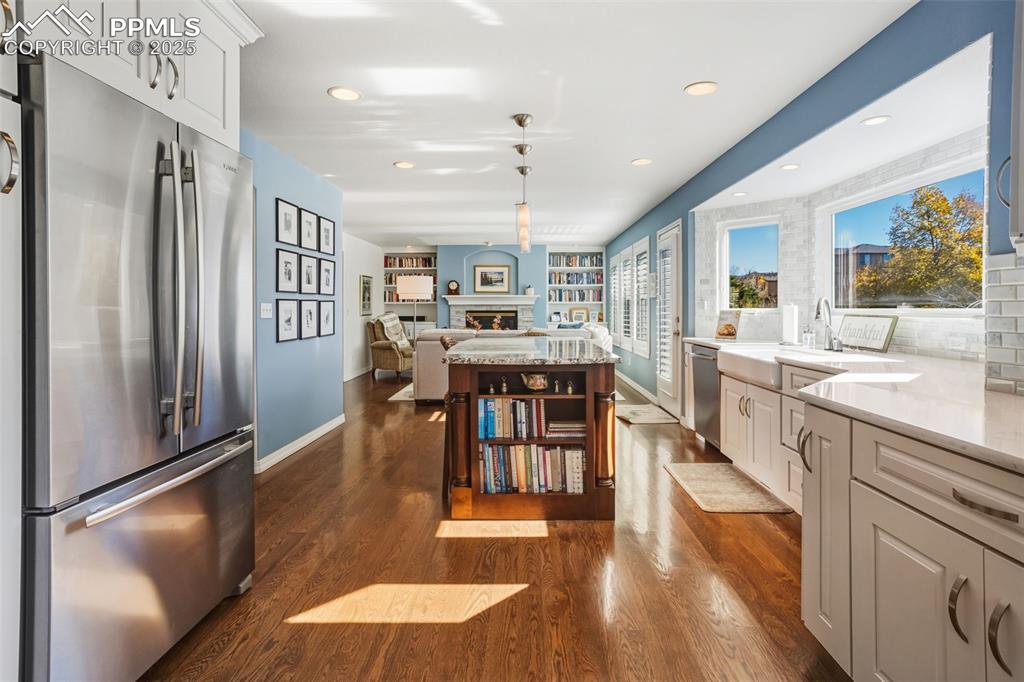 Kitchen with stainless steel appliances, dark wood-style floors, a fireplace, light stone countertops, and recessed lighting