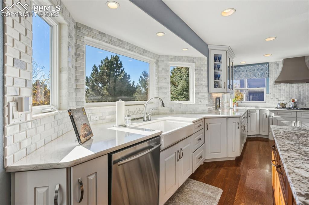 Kitchen with backsplash, dishwasher, dark wood finished floors, light stone countertops, and recessed lighting