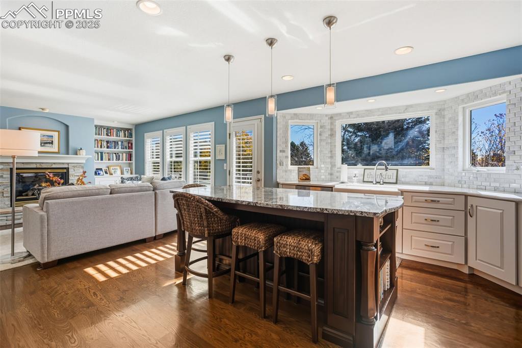 Kitchen with a breakfast bar area, light stone countertops, decorative light fixtures, dark wood-style floors, and recessed lighting