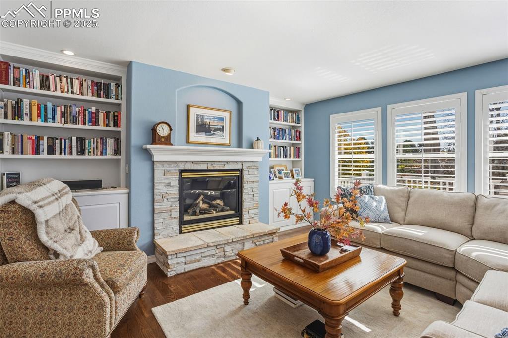 Living room with dark wood-type flooring, a stone fireplace, built in shelves, and recessed lighting