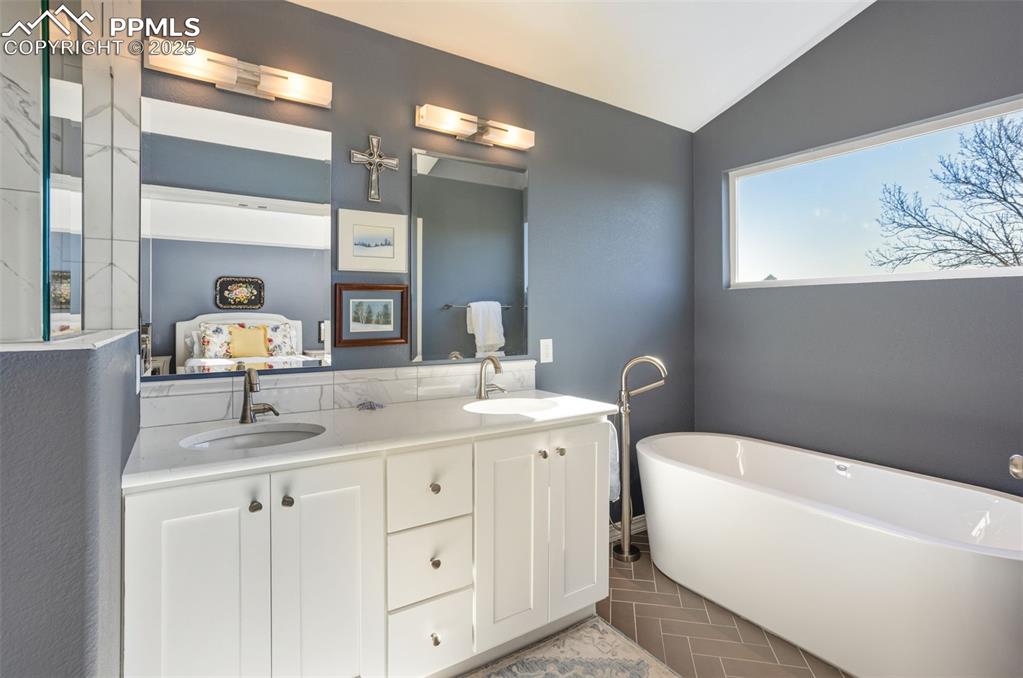 Bathroom featuring vaulted ceiling, double vanity, a freestanding bath, ensuite bathroom, and light tile patterned flooring