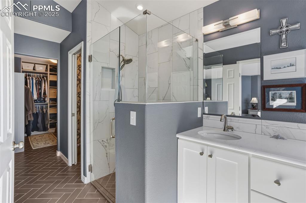 Bathroom featuring vanity, a walk in closet, and a marble finish shower