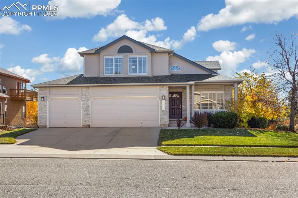 Traditional home featuring a front lawn, concrete driveway, a garage, and roof with shingles