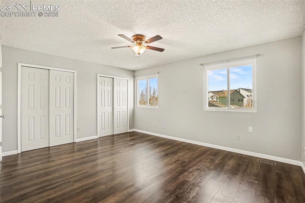 Unfurnished bedroom featuring multiple closets, dark wood finished floors, a ceiling fan, and a textured ceiling