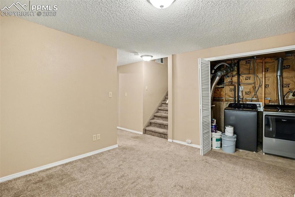 Finished below grade area with a textured ceiling, carpet, and washer and clothes dryer