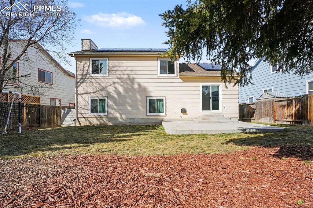 Rear view of house featuring solar panels, a chimney, a fenced backyard, and a patio